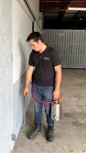 Exterminateur arrosant le bas d'un mur.